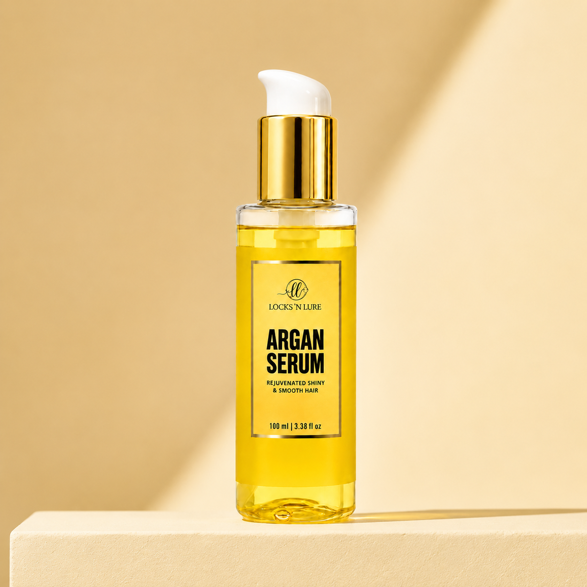 A bottle of Lock 'N Lure Argan Serum, a golden-yellow hair oil with a white pump and gold collar, displayed on a beige pedestal against a matching beige background with soft diagonal shadows.