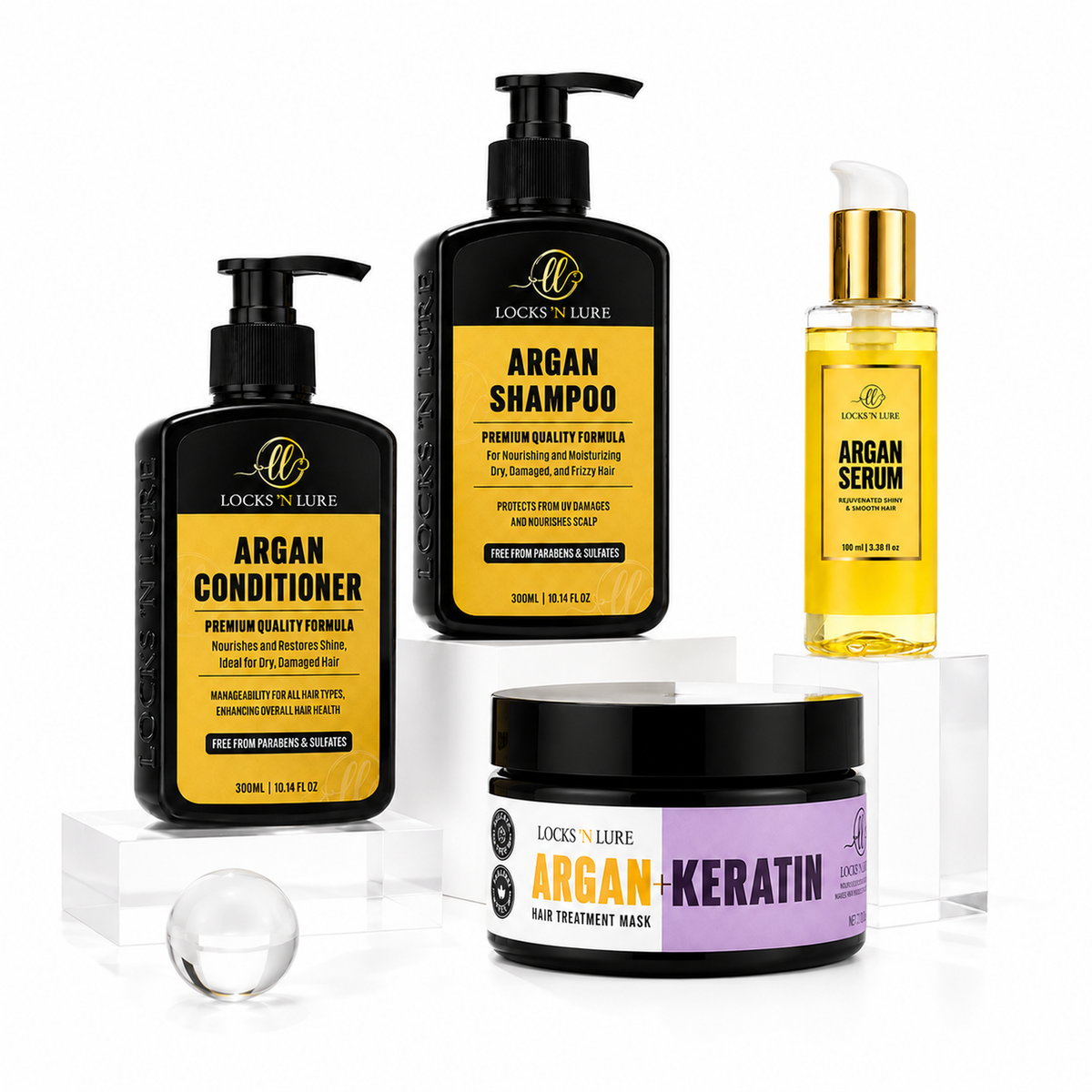 Four Lock's Luxe haircare products arranged on clear acrylic blocks against a white background: Argan Conditioner, Argan Shampoo, Argan Serum, and an Argan+Keratin hair treatment mask jar. The bottles and jars are black with yellow and lavender labels, and one bottle has a gold cap.