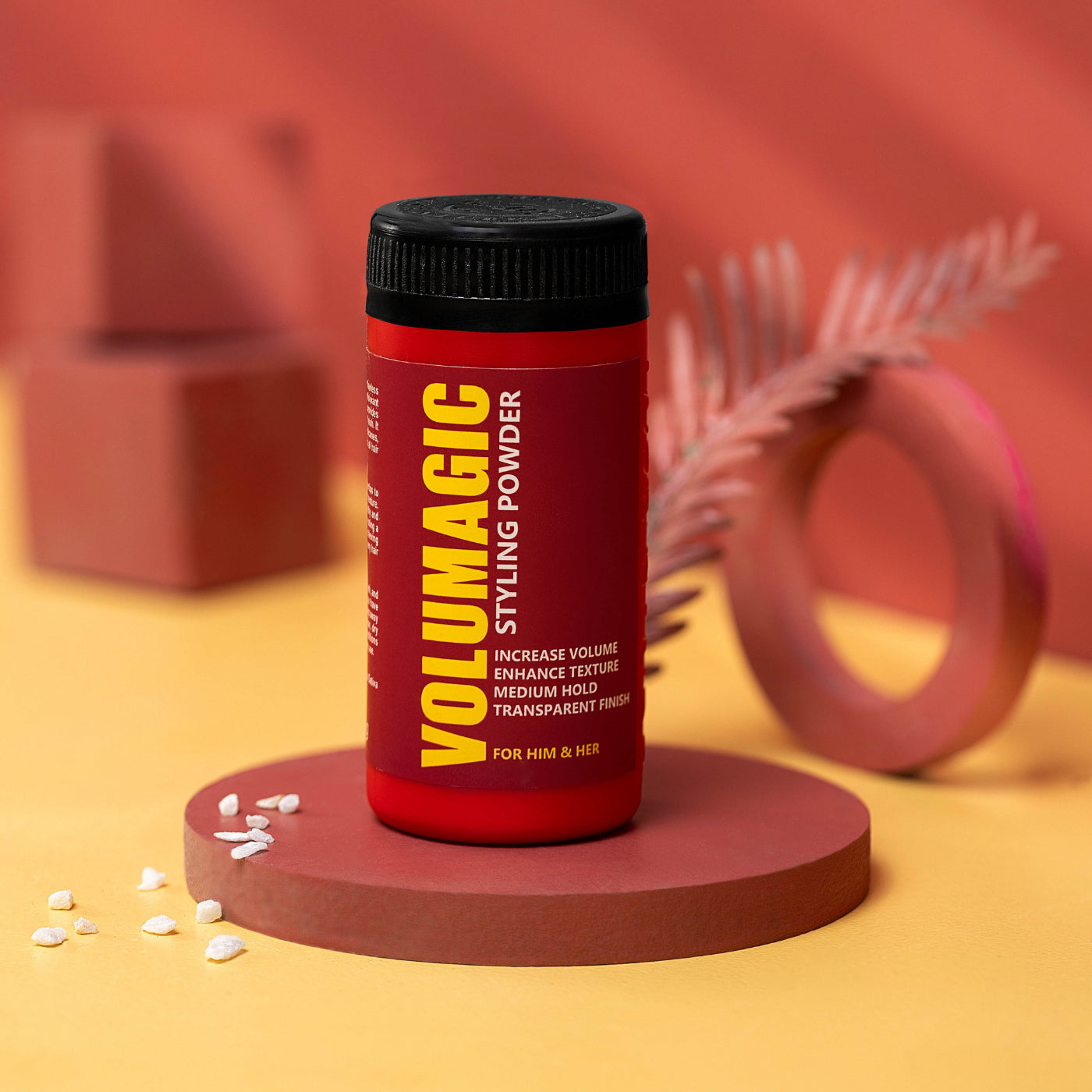Red bottle of Volumagic styling powder on a pink platform with a blurred background
