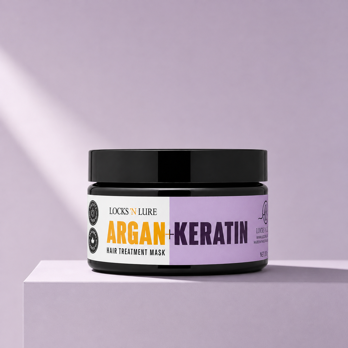 A jar of Locks 'N Lure Argan + Keratin Hair Treatment Mask sits on a matching lavender pedestal. The product container is black with a white and lavender label featuring orange and purple text.