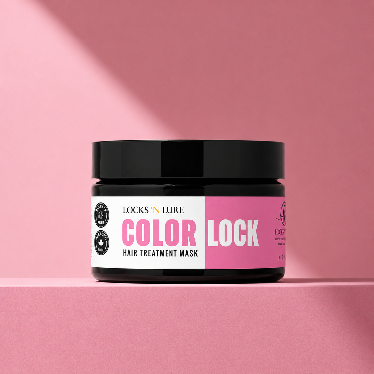 A jar of Locks N Lure Color Lock Hair Treatment Mask on a pink platform with a pink background. The jar has a black lid and a white and pink label.