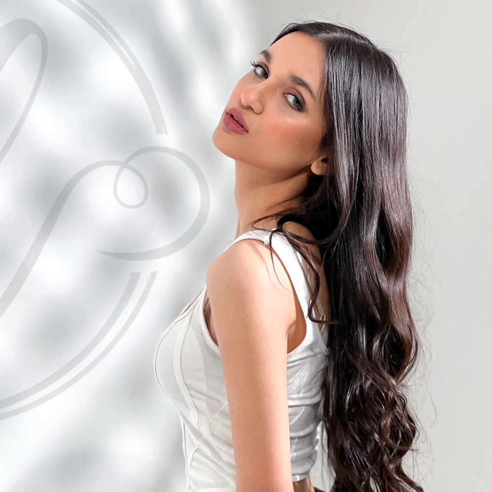 Woman with long dark hair wearing a white sleeveless top against a light gray background